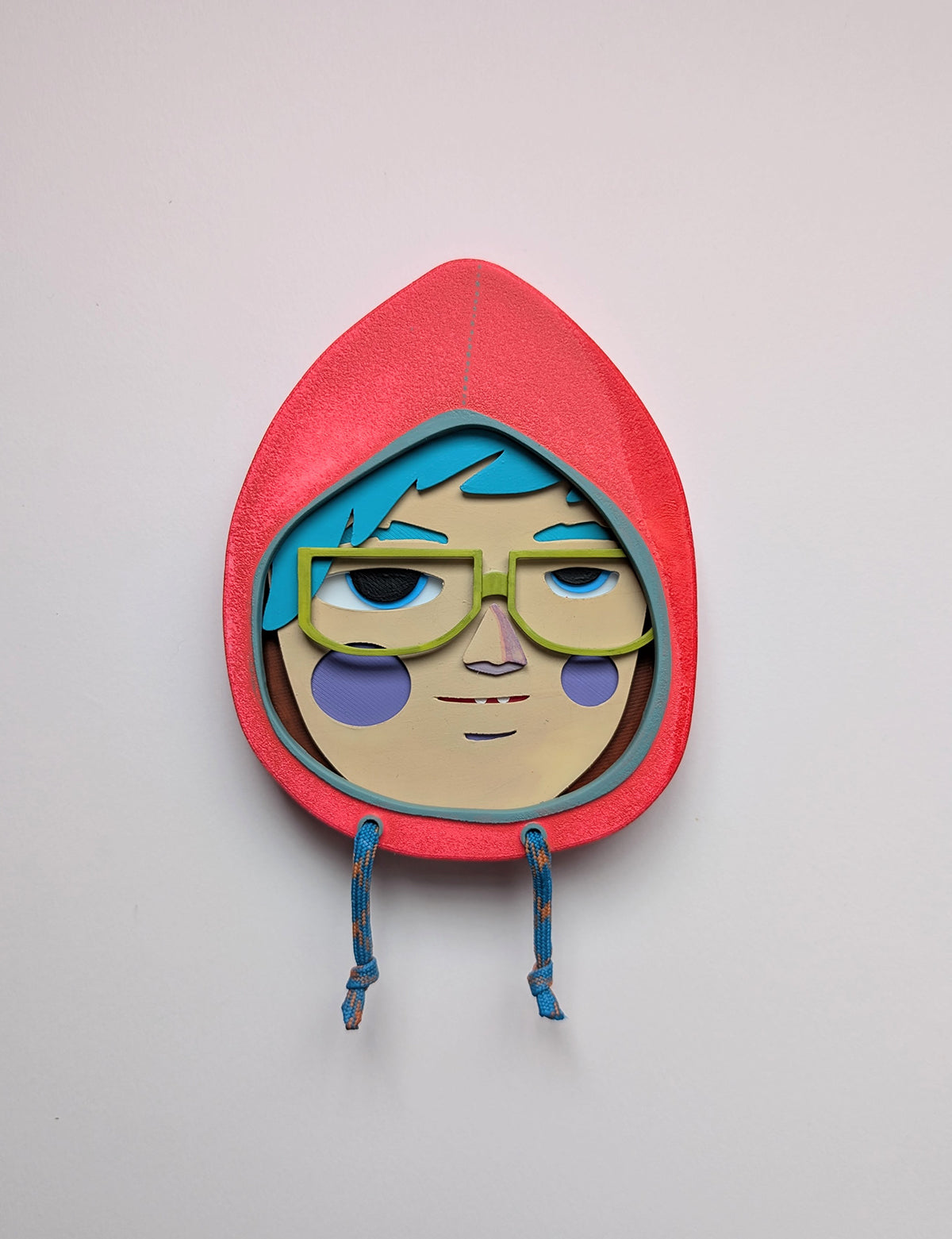 Front view of a bright orange colored hoodie shaped wall sculpture featuring teal hair, yellow green glasses, and purple cheeks on a white background.