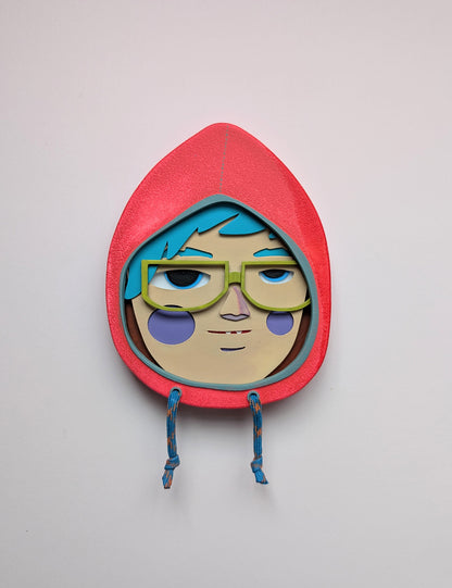 Front view of a bright orange colored hoodie shaped wall sculpture featuring teal hair, yellow green glasses, and purple cheeks on a white background.