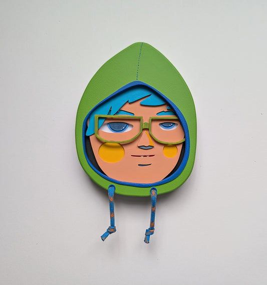 Yellow green in color hooded wall sculpture with teal hair, green glasses hung on a white wall.