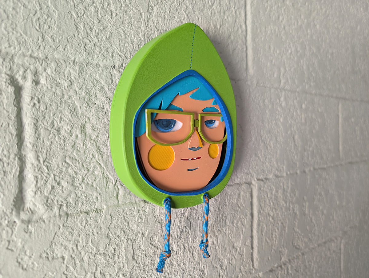A side view showing depth of a yellow green in color hooded wall sculpture with teal hair, green glasses hung on a brick wall.