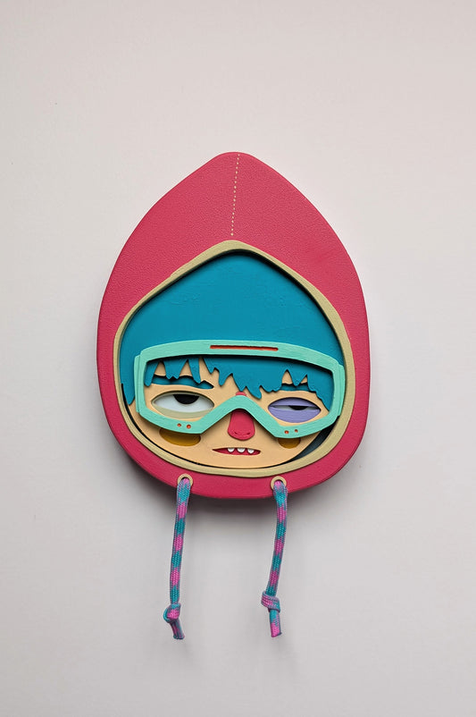 Magenta color wall sculpture featuring a character in a hoodie with teal hair, mint goggles, hung on a white wall.