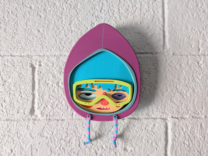 A purple hooded wall sculpture that has blue hair, bright yellow green googles on brick wall