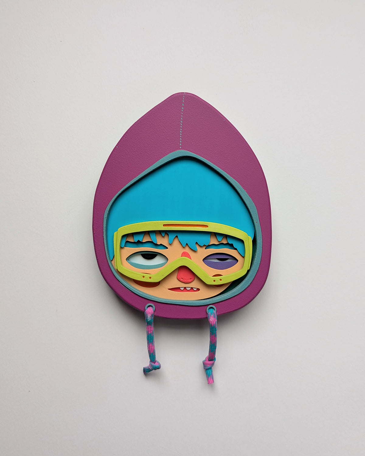 Purple hooded wall sculpture that has blue hair, bright yellow green googles on a white wall