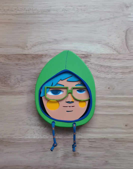 A video showing size and depth of a yellow green in color hooded wall sculpture with teal hair, green glasses with a wood table in the background.