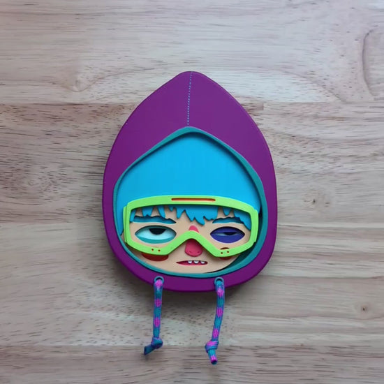 A video of a purple hooded wall art sculpture showing art size and depth with a wood table in the background.